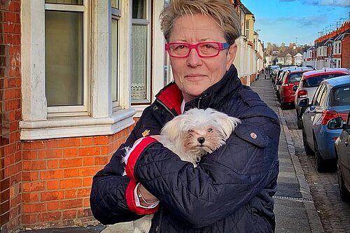 Ana Savage Gunn standing on a terraced street holding a small white dog