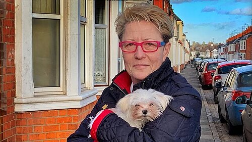 Ana Savage Gunn standing on a terraced street holding a small white dog