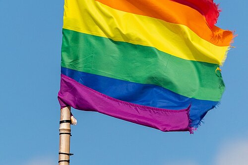 The LGBTQ+ rainbow flag against a blue sky